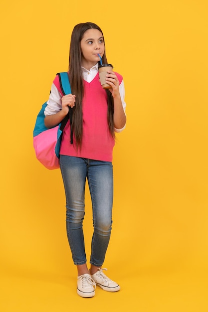 Menina da escola adolescente feliz com mochila bebida cacau para viagem em fundo amarelo, escola.