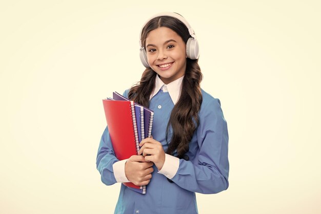 Menina da escola adolescente usando fones de ouvido lendo um livro sobre fundo branco isolado