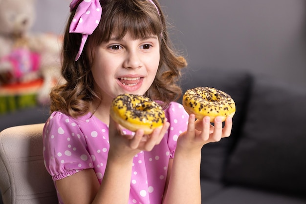 Menina da escola alegre brincando com bolos dentro de casa menina adolescente engraçada se divertindo com rosquinhas coloridas