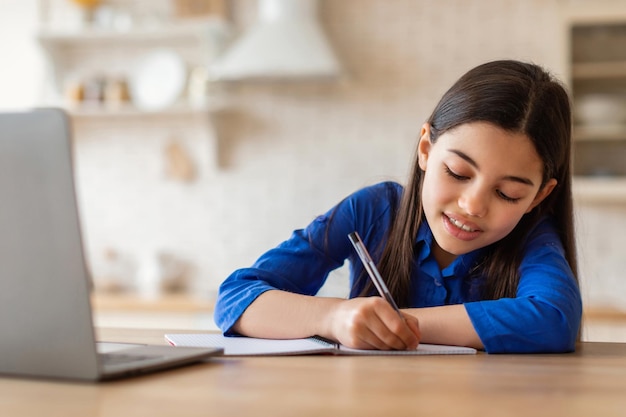 Menina da escola aprendendo com laptop em casa e fazendo anotações