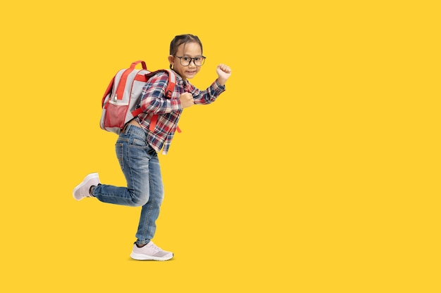 Menina da escola Feliz estudante asiática com mochila e caminhando Retrato de corpo inteiro isolado em fundo amarelo com traçado de recorte para trabalho de design