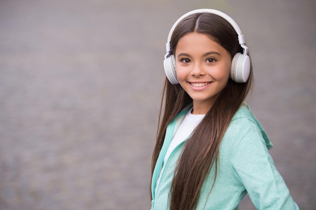 Menina da escola feliz ouve música ou livro de áudio em fones de ouvido para educação e alegria, novas tecnologias, espaço de cópia.