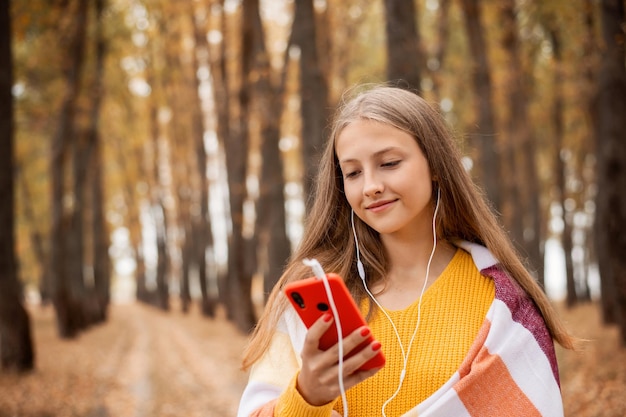 Menina da escola feliz ouvindo música na floresta de outono colorida