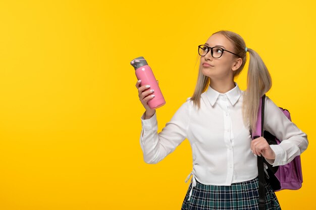 Menina da escola loira do dia mundial do livro segurando o frasco rosa e mochila