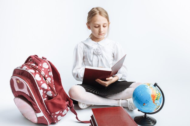 Menina da escola menina bonitinha sentada com livros e um globo, lendo um livro