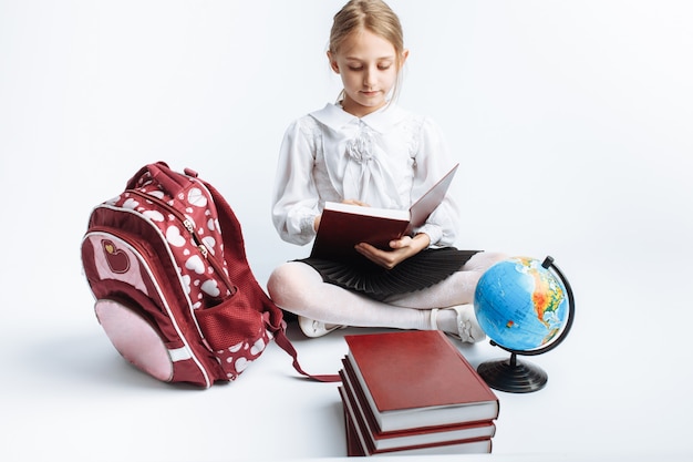 Menina da escola menina bonitinha sentada com livros e um globo, lendo um livro