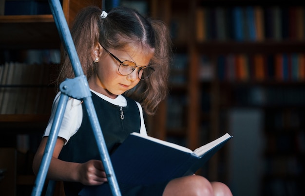 Menina da escola na escada em uma biblioteca cheia de livros