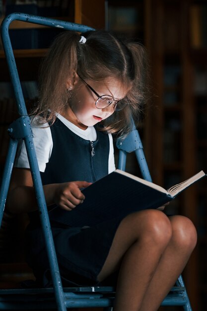 Menina da escola na escada em uma biblioteca cheia de livros