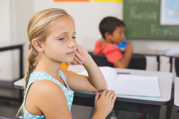 Foto menina da escola pensativa, sentado na mesa com a mão no rosto