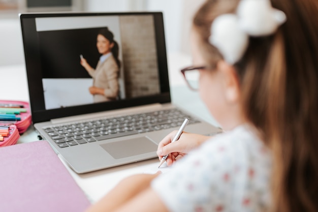 Menina da escola primária jovem assistindo aula de educação online. conceito de educação de bloqueio de coronavirus ou covid-19.