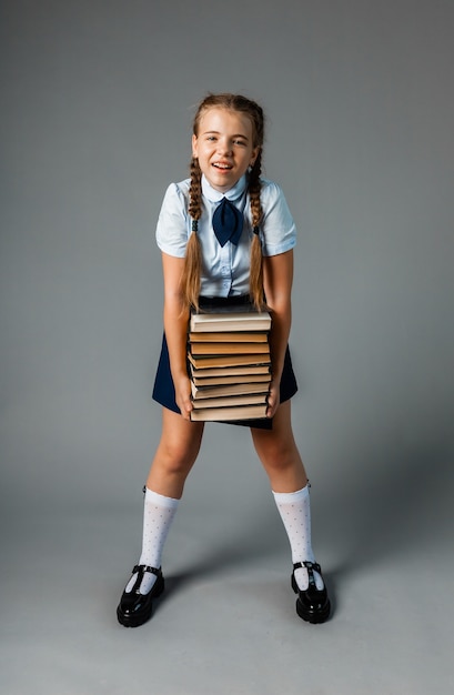 Menina da escola segurando livros pesados sobre fundo amarelo do estúdio