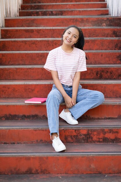 Menina da escola usa camisa rosa e jeans segurando e segurando livro rosa nas escadas