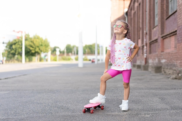 Menina da moda em óculos de sol com skate rosa na cidade