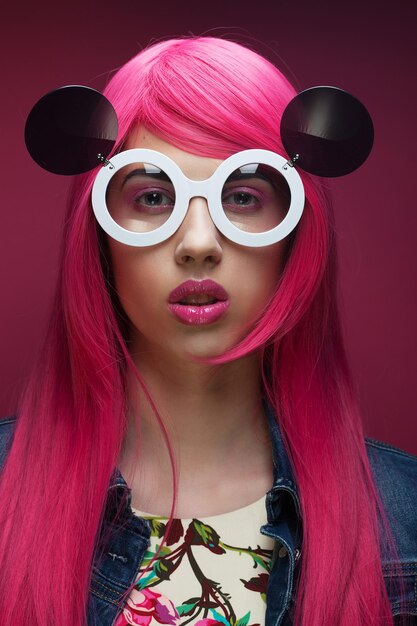 Menina da moda jovem com cabelo rosa e óculos de sol grandes sobre fundo rosa