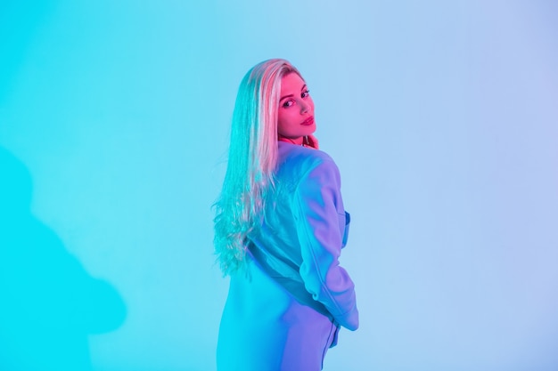 Menina da moda jovem modelo de negócios com casaco azul olhando para a câmera em cores pastel luzes neon rosa no estúdio
