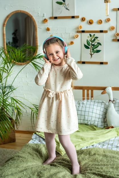 Menina dança na cama em fones de ouvido bebê gosta de ouvir música via conexão sem fio