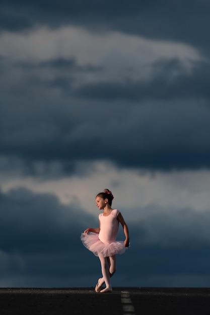 Menina dançarina de balé vestindo um tutu rosa posando no horizonte da estrada ao pôr do sol