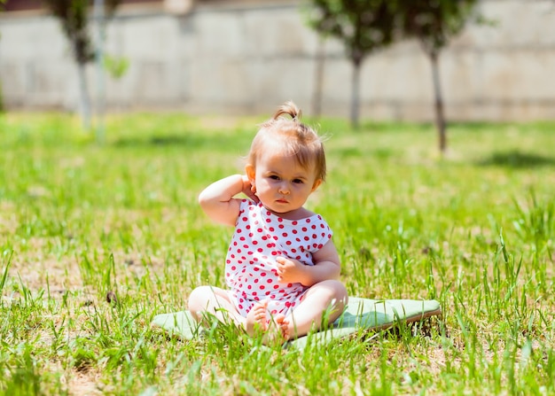 Menina de 11 meses de idade está sentada no parque na grama. menina com um casaco de ervilhas senta-se na grama e brinca com bolhas de sabão.