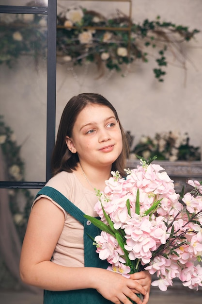 menina de 12 anos de vestido verde com flores cor de rosa nas mãos