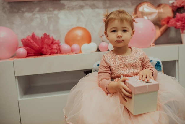 Menina de 2 anos de vestido rosa com seu primeiro bolo de aniversário feliz aniversário carda menina bonitinha comemora seu primeiro aniversário cercada de presentes