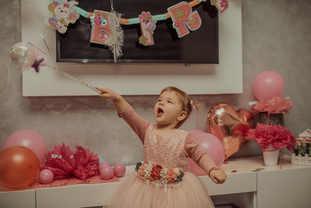 Menina de 2 anos de vestido rosa com seu primeiro bolo de aniversário feliz aniversário carda menina bonitinha comemora seu primeiro aniversário cercada de presentes