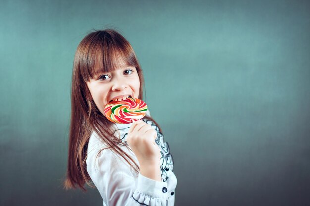 Menina de 6 ou 7 anos comendo um grande pirulito multicolorido