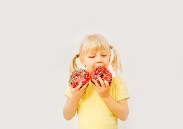 Menina de bebê fofo comendo rosquinhas doces sobre um fundo claro.