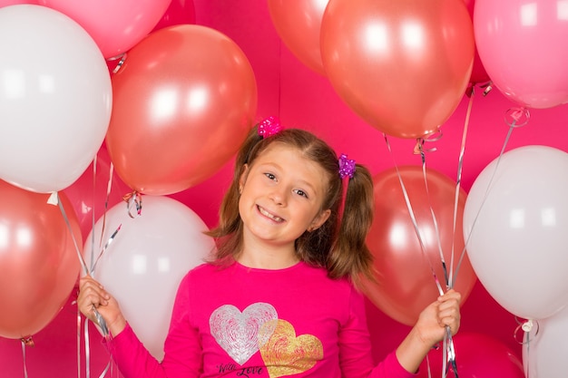 Menina de beleza com balões de ar coloridos sorrindo sobre fundo rosa.