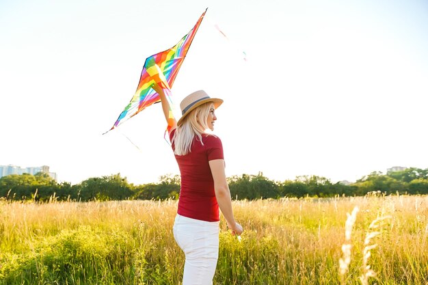 Menina de beleza correndo com pipa no campo. Mulher jovem e bonita com pipa colorida sobre céu azul claro. Livre, conceito de liberdade. Emoções, estilo de vida saudável