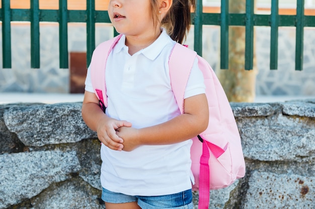 Menina de cabelo preto com uma mochila rosa vai para a escola