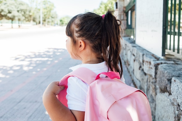 Foto menina de cabelo preto com uma mochila rosa vai para a escola