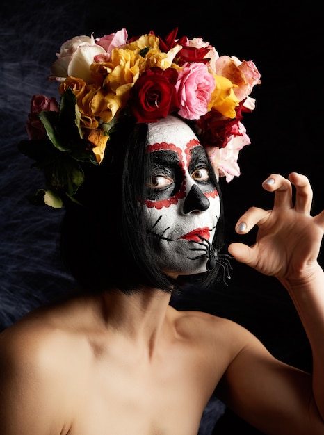 Menina de cabelo preto está vestida com uma coroa de rosas multicoloridas e maquiagem é feita no rosto caveira de açúcar para o dia dos mortos