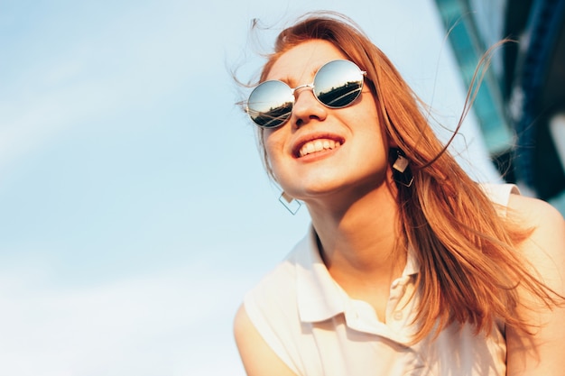 Foto menina de cabelo vermelha feliz bonita positiva nos óculos de sol do espelho