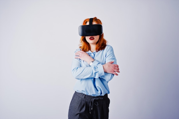 Menina de cabelo vermelha na blusa azul com os vidros do vr isolados no branco.