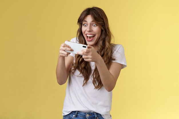 Menina de cabelos cacheados entusiasmada alegre otimista, tentando jogar um jogo incrível incrível para smartphone ...