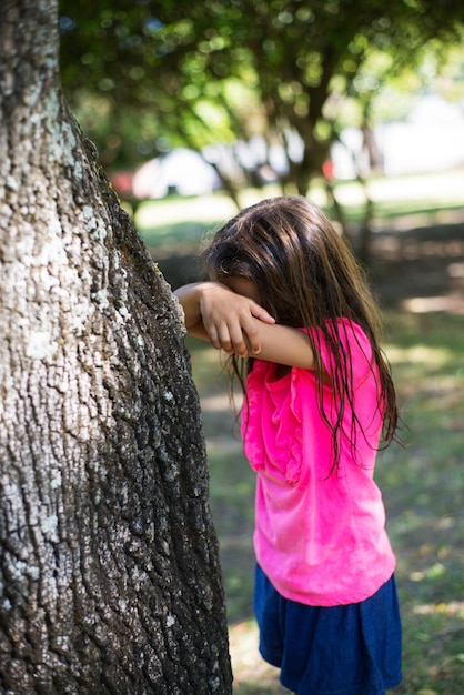 Foto menina de cabelos compridos brincando no parque. garota de cabelos escuros brincando de esconde-esconde, contando. família, amor, conceito de infância