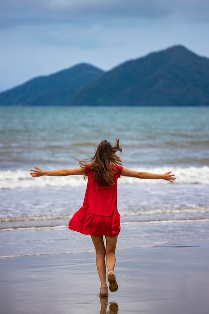 menina de cabelos compridos de vestido vermelho caminha ao longo da praia tropical australiana com ilhas ao fundo