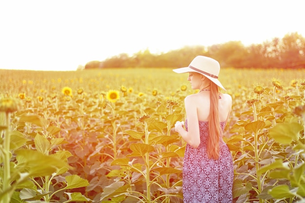 Menina de cabelos compridos fica no contexto do ensolarado campo de girassol florescendo