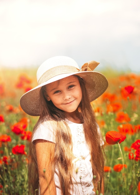 Menina de cabelos compridos no chapéu posando no campo de papoulas com sol de verão Vertical