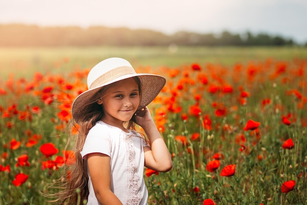 Menina de cabelos compridos no chapéu posando no campo de papoulas com sol de verão