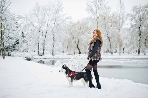 Menina de cabelos vermelha andando no parque com cães husky em dia de inverno.