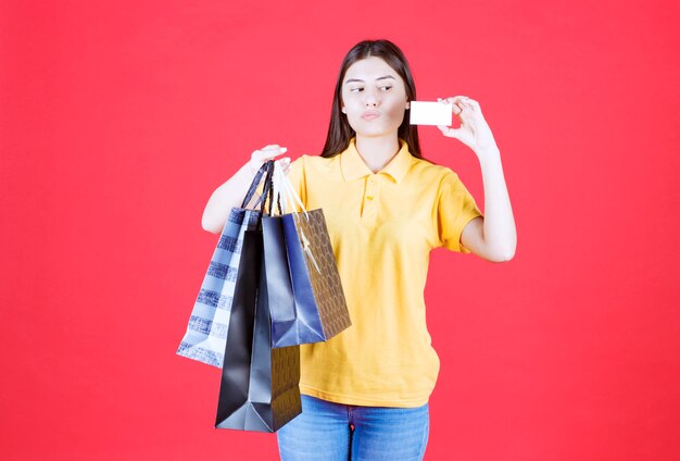Menina de camisa amarela segurando várias sacolas de compras azuis e apresentando seu cartão de visita