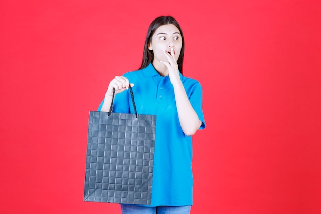 Menina de camisa azul segurando uma sacola roxa e parece emocionada e estressada.