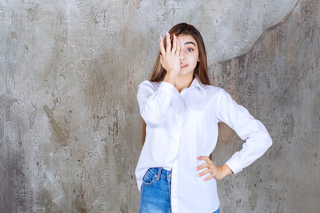 Menina de camisa branca em pé em uma parede de concreto e se sentindo assustada e apavorada.