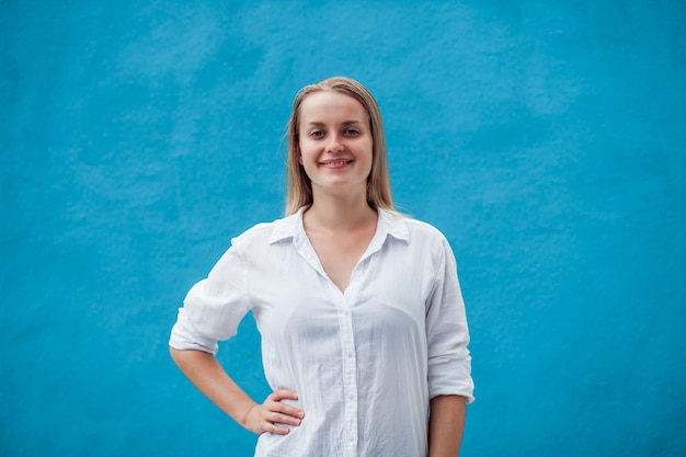 Menina de camisa branca na parede azul sorrindo