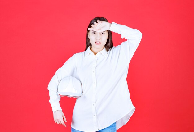 Menina de camisa branca segurando um capacete branco e parece cansada