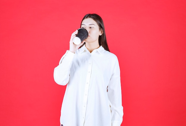 Menina de camisa branca segurando uma xícara de café preta para viagem