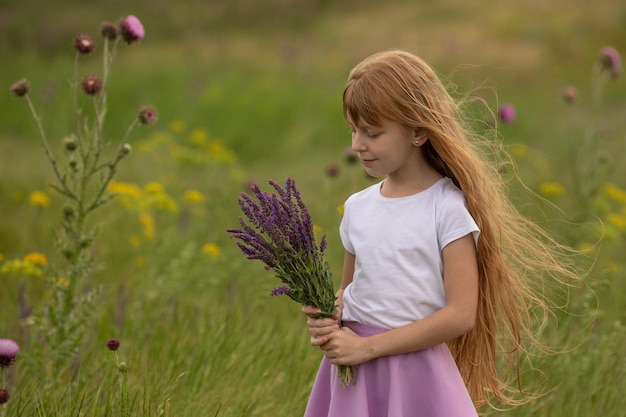 Menina de camiseta branca segura um buquê de flores silvestres em um prado