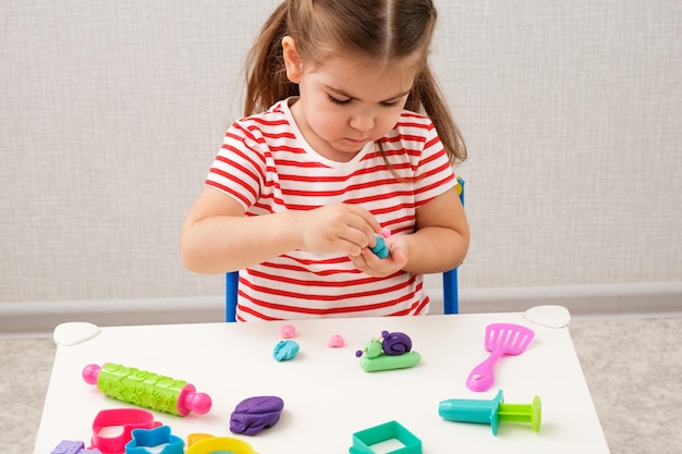 Menina de camiseta listrada brilhante brincando com plasticina fazendo caracóis na mesa branca conceito de jogos educacionais em casa