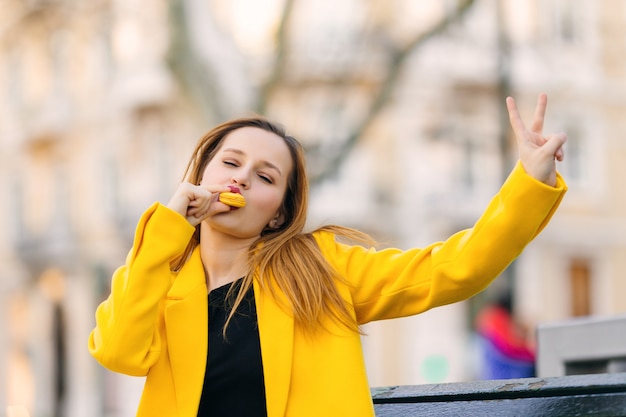 Menina de casaco amarelo come biscoito amarelo e mostra um gesto